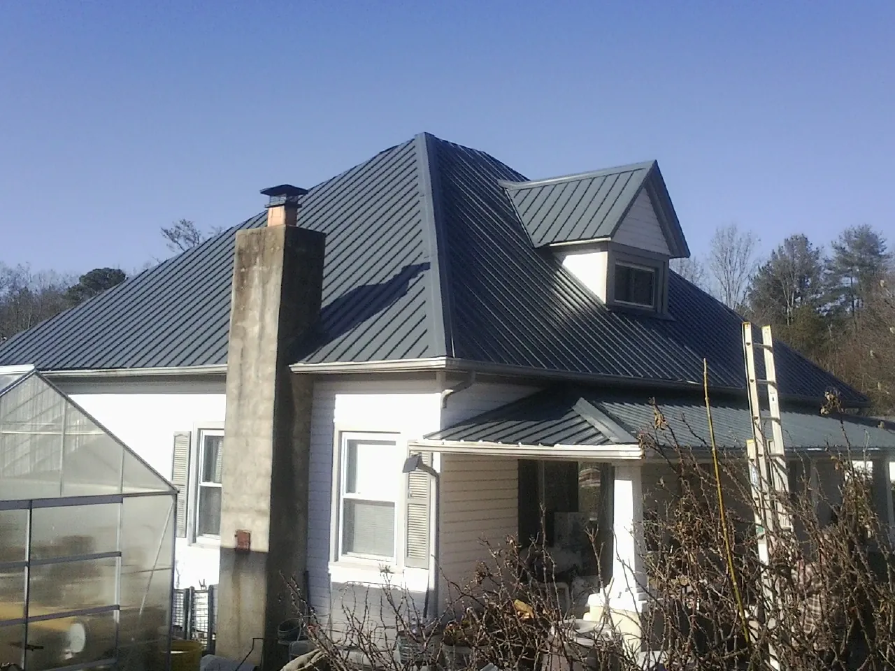 Dark blue standing seam metal roof on a white farmhouse with dormer — Slate & Tile Roof Repair by Roofing Brothers in Conley