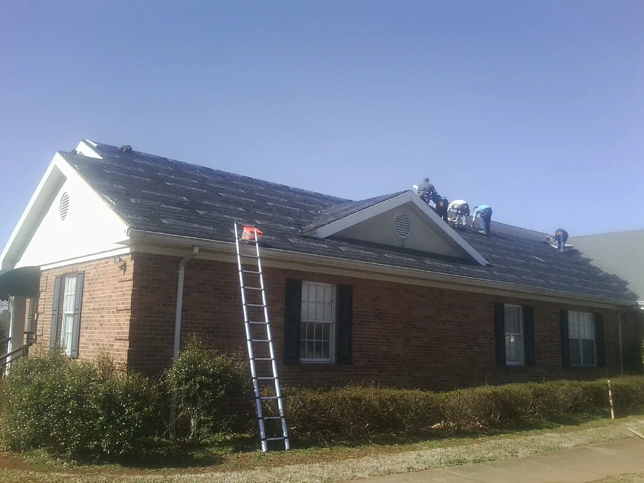 Crew tearing shingles off a brick ranch roof with a ladder set — Emergency Roof Repair work by our crew in Conley