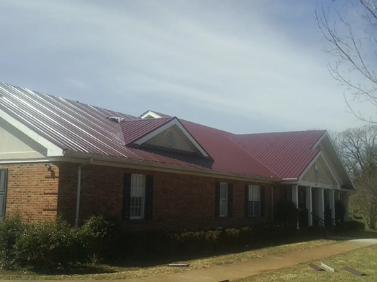 Red metal roof with gabled entries on a long brick building, from a Hail Damage Roof Repair job in Conley