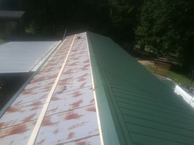 Old rusted panels beside newly installed green metal roofing — Wind Damage Roof Repair by Roofing Brothers in Conley