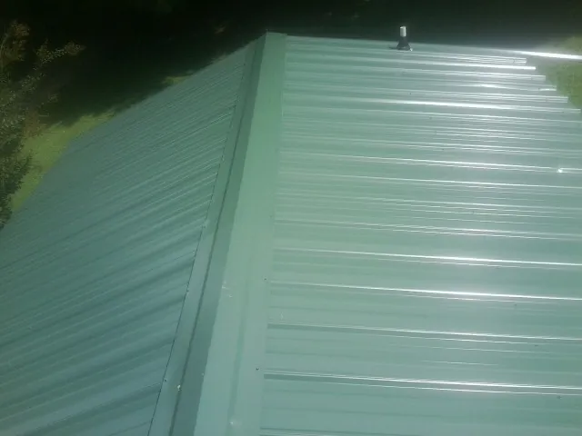 New green metal panels meeting at the ridge of a roof — Flat Roof Repair work by our crew in Conley