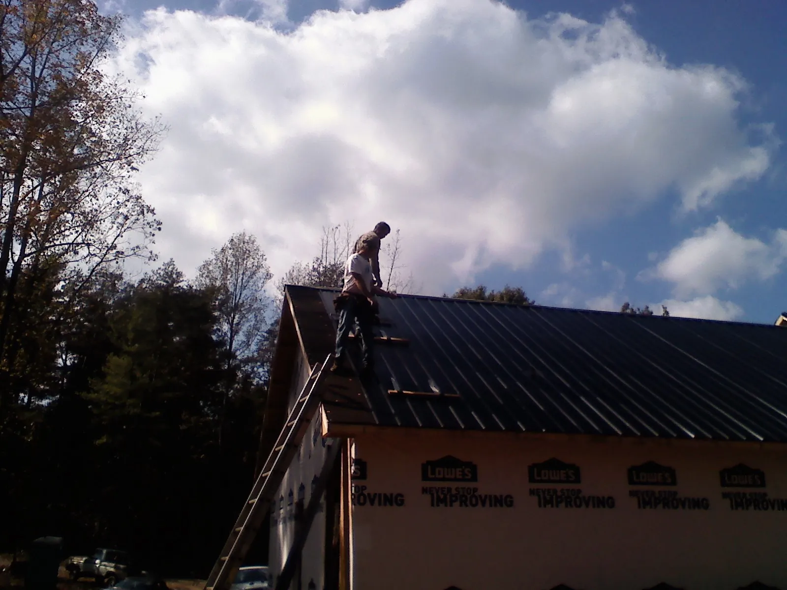 Roofer fastening dark metal panels high against a cloudy sky, from a Roof Inspection job in Conley