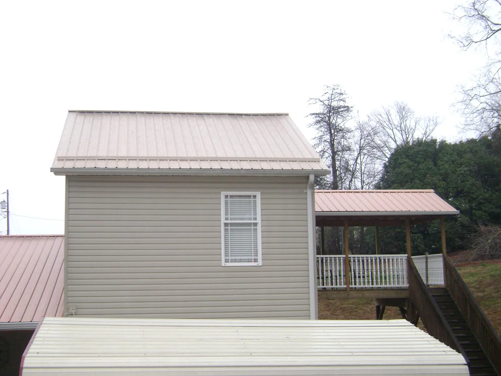 Tan metal roofs on a two story addition and attached porch, from a Roof Replacement job in Conley